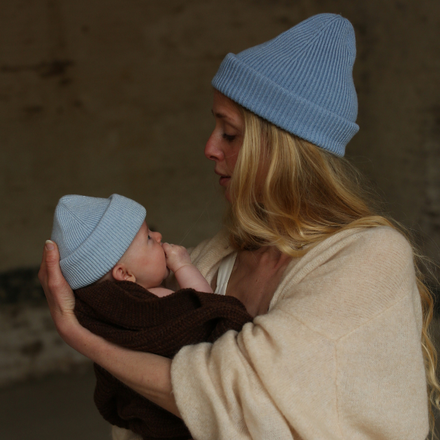 Baby draagt de Hvid newborn beanie Fonzie in Sky van merinowol, bij De Gele Flamingo.