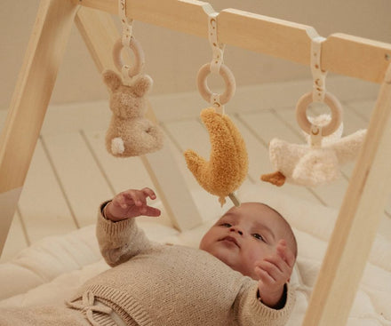Baby ligt onder de Little Dutch babygym Newborn Naturals met hangspeeltjes