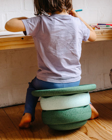 Stapelstein Balance Board Dark Green, kind zit aan tafel op een kruk van stenen en bord