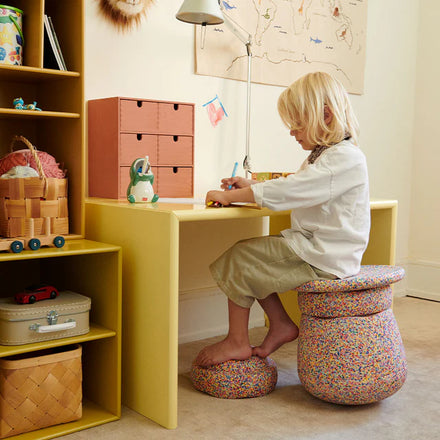 Stapelstein Base Super Confetti, kind zit op de Base aan een geel bureau
