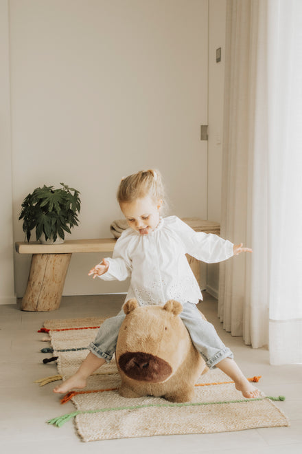 Wild & Soft Bouncy Capybara, meisje houdt haar evenwicht met gespreide armen, blik omlaag