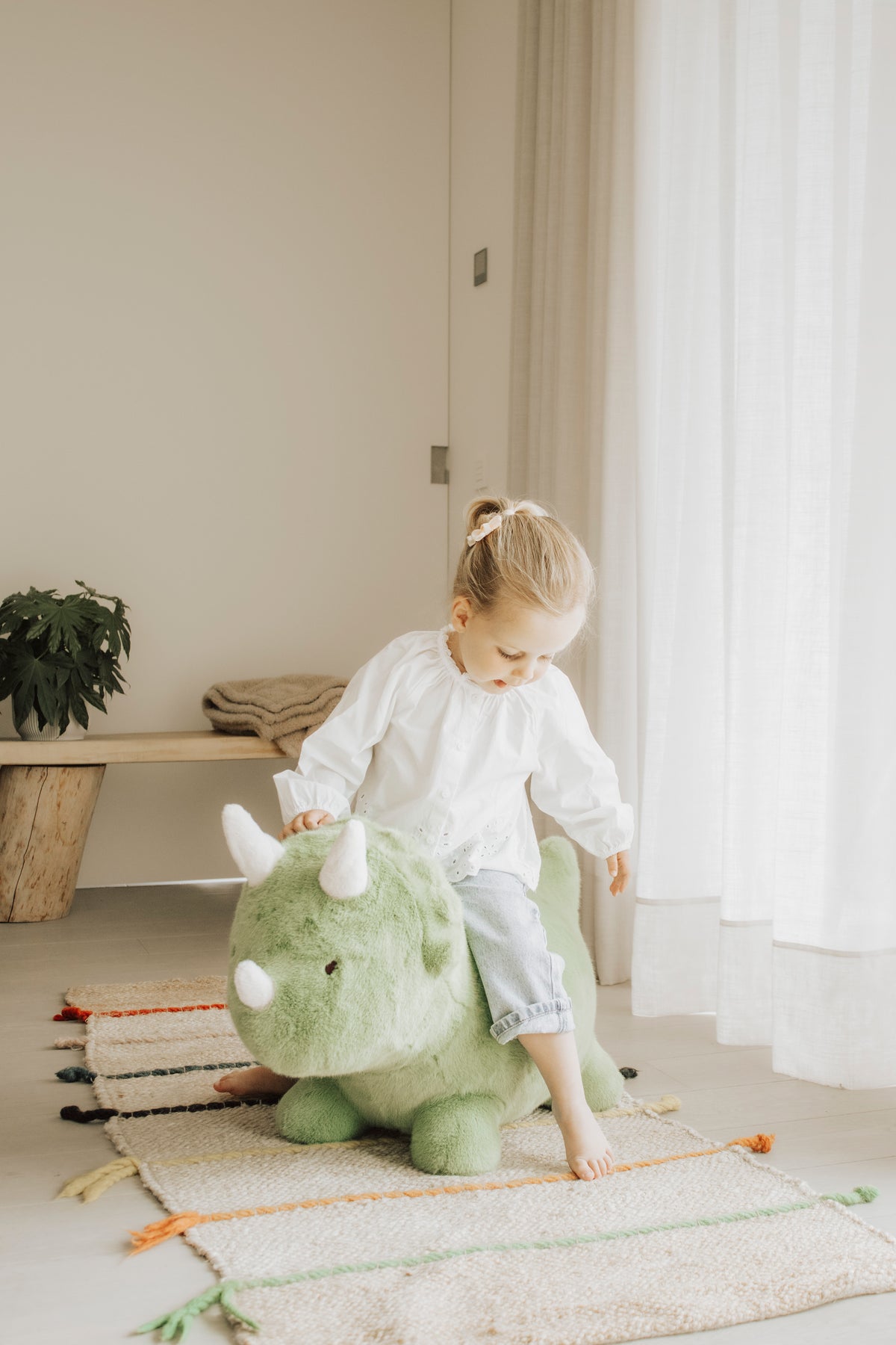 Wild & Soft Bouncy Dino, meisje zit lachend op de groene dino met witte hoorns