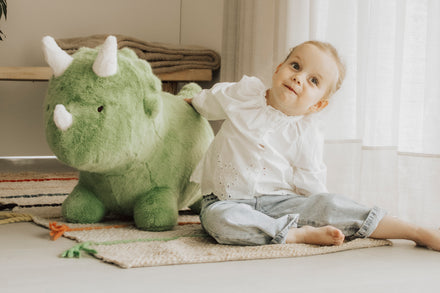 Wild & Soft Bouncy Dino, meisje leunt lachend tegen de groene dino op het tapijt