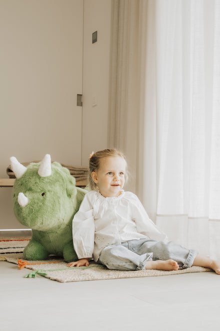 Wild & Soft Bouncy Dino, meisje zit naast de groene dino in een lichte kamer, staand beeld