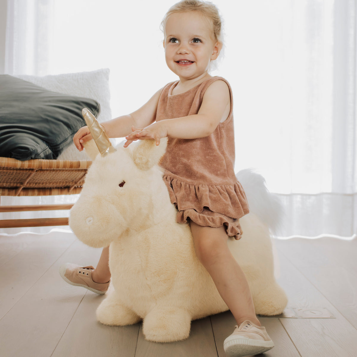 Wild & Soft Bouncy Eenhoorn, meisje zit lachend op de crèmekleurige eenhoorn