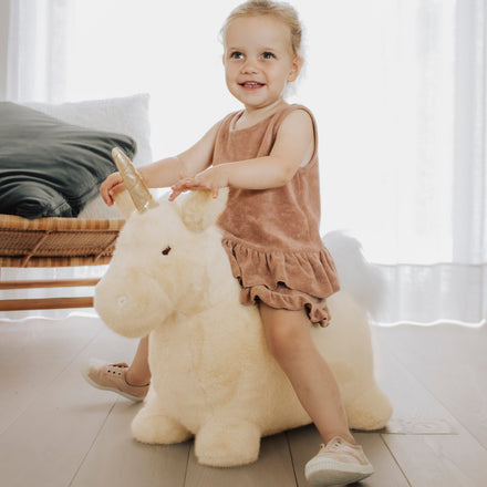 Wild & Soft Bouncy Eenhoorn, meisje zit lachend op de crèmekleurige eenhoorn