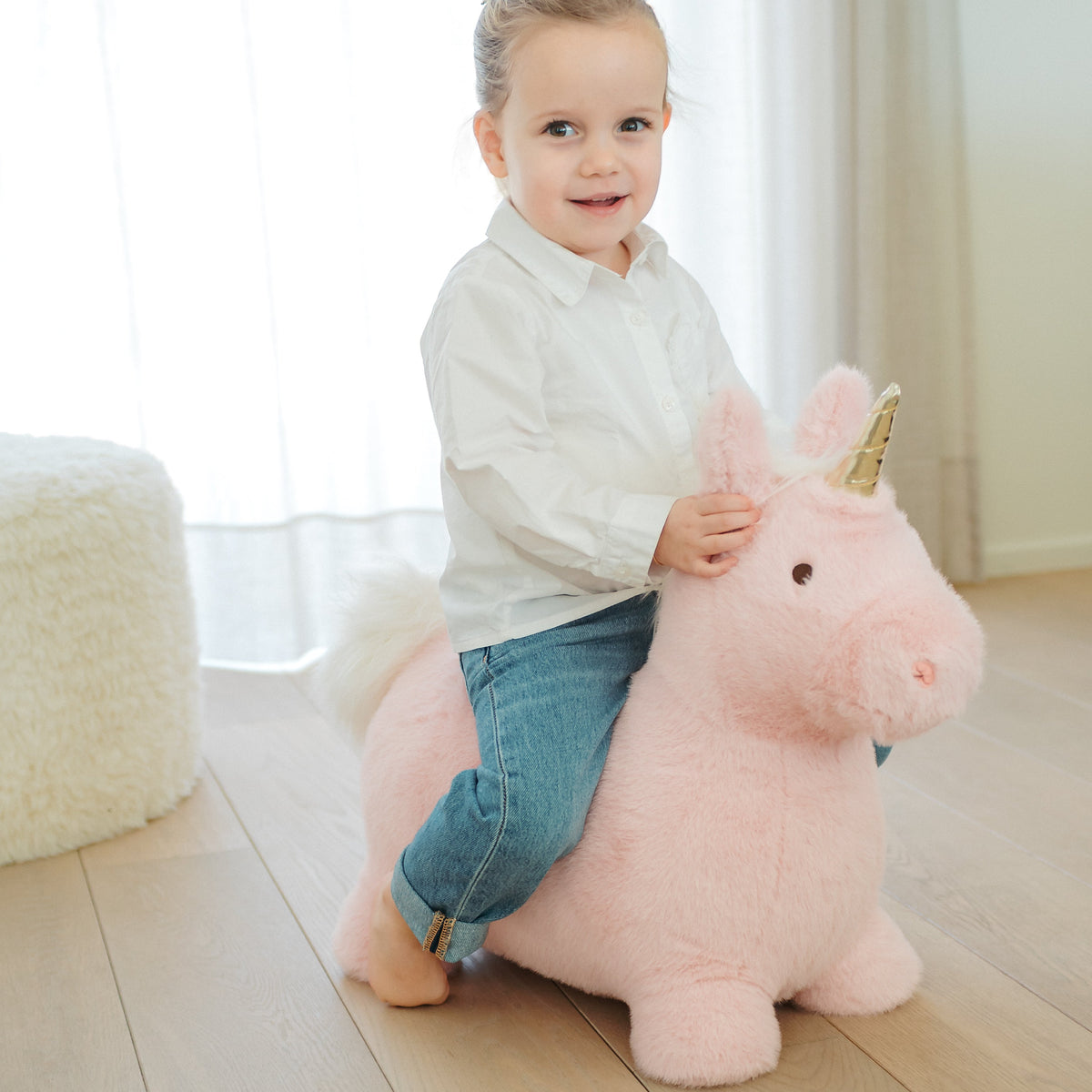 Wild & Soft Bouncy Roze Eenhoorn, jongen zit lachend op de roze eenhoorn naast een witte poef