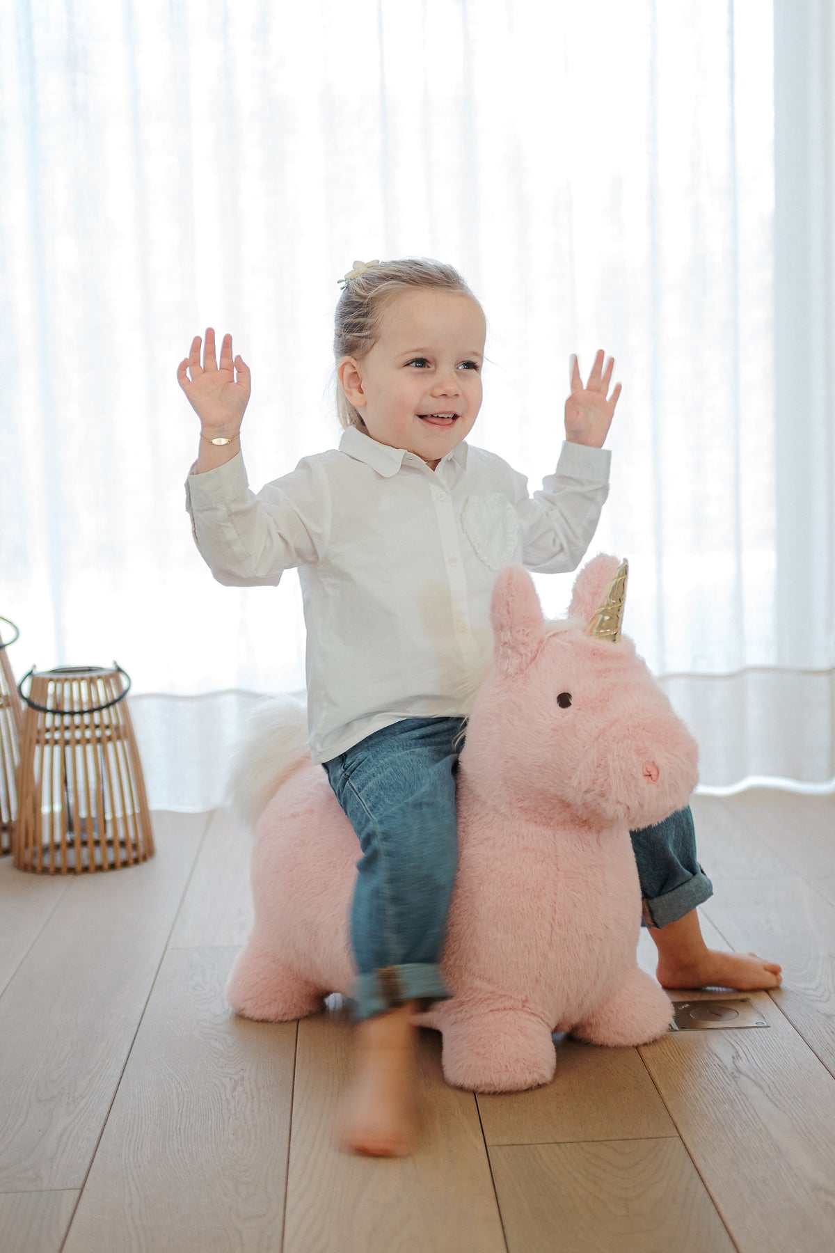 Wild & Soft Bouncy Roze Eenhoorn, jongen zit lachend op de roze eenhoorn naast een witte poef